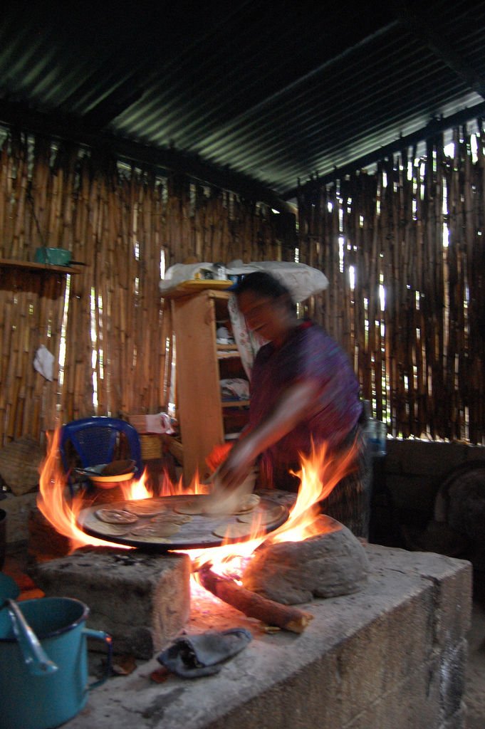 Mujer haciendo tortillas sobre comal calentado con leña